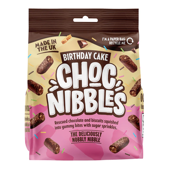 Close-up of a Chocolate Nibbles Birthday Cake (135g) from a 12‑pack — moist chocolate sponge with glossy chocolate icing and multicolored sprinkles, retail packaging visible