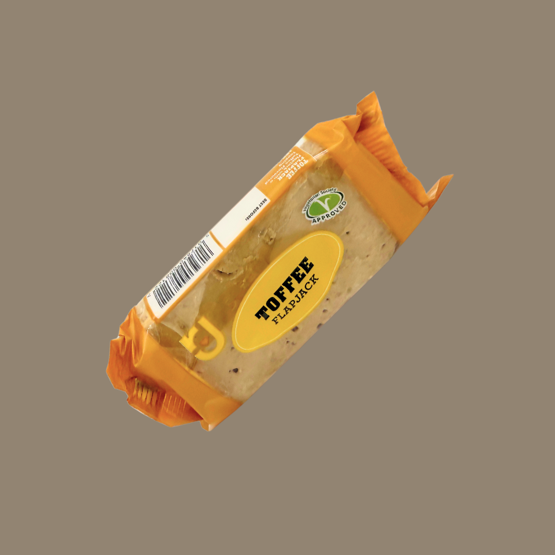 Hand holding a toffee flapjack over a picnic blanket with berries