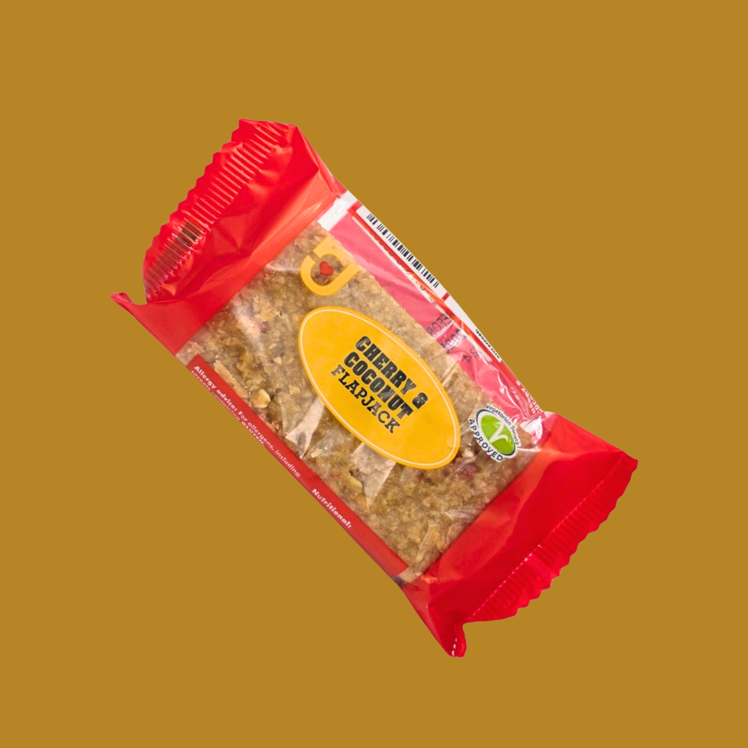 Hand holding a Cherry & Coconut flapjack bar over a beach towel