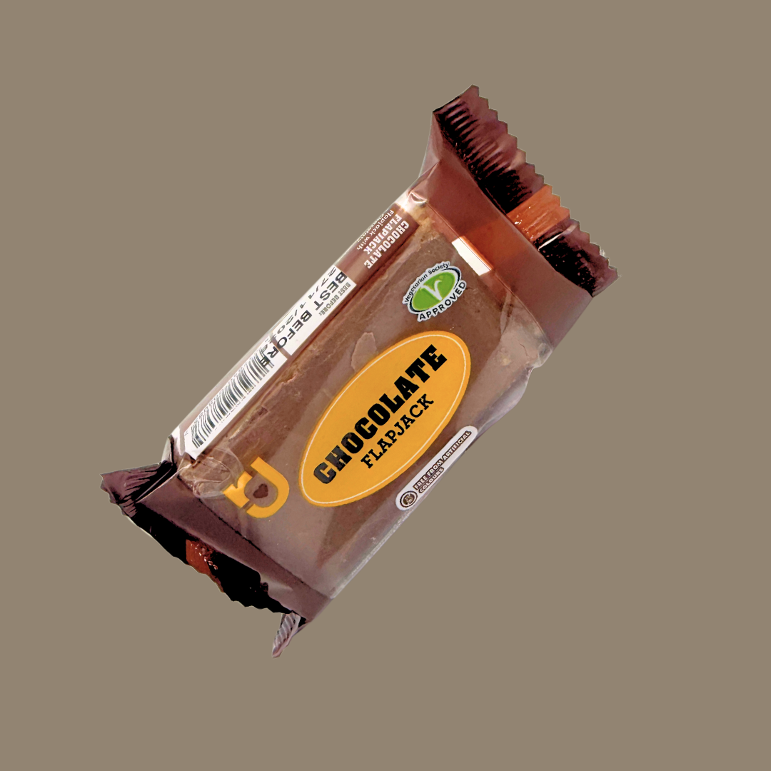 Hand holding a chocolate flapjack over a picnic spread