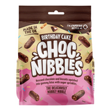 Close-up of a Chocolate Nibbles Birthday Cake (135g) from a 12‑pack — moist chocolate sponge with glossy chocolate icing and multicolored sprinkles, retail packaging visible