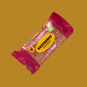 Hand holding a raspberry flapjack bar over a picnic blanket with berries
